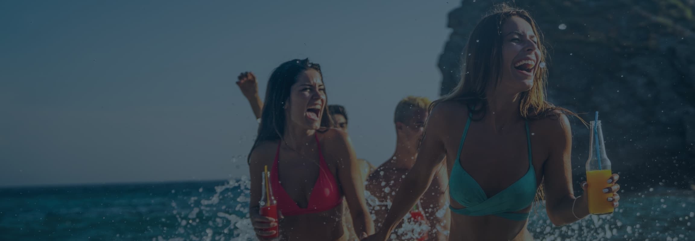 Friends running through the surf at sunset with drinks in hand